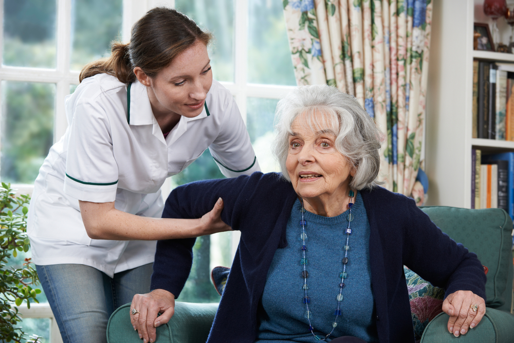 Fysiotherapeute helpt stijve oude vrouw op te staan uit stoel.