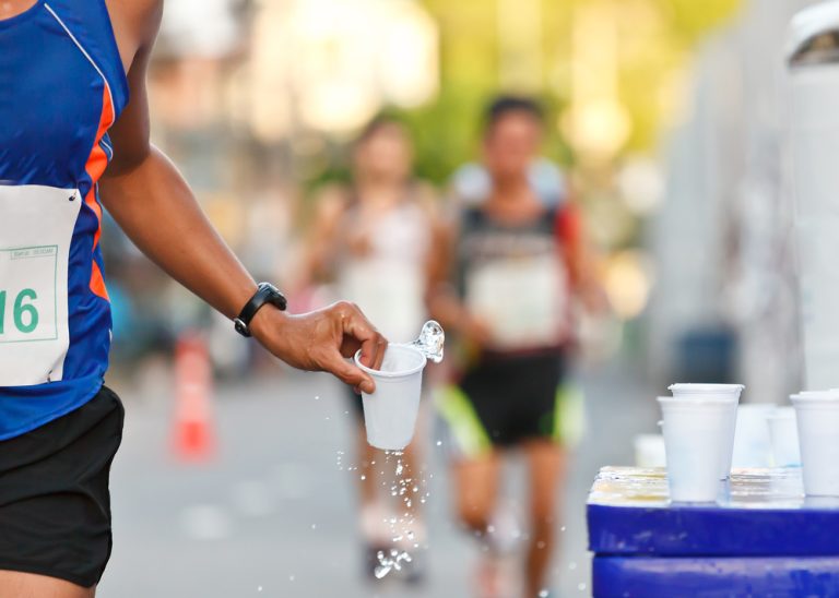 12-13-Voeding en drinkstrategieën tijdens het hardlopen_107608997 Hardloper pakt tijdens een wegwedstrijd en bekertje water.