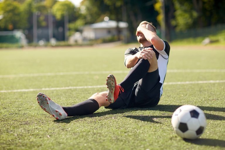 12-14-Psychologische programma’s verminderen risico op voetbalblessures_570884644 Voetballer ligt geblesseerd op de grond en grijp naar zijn knie.