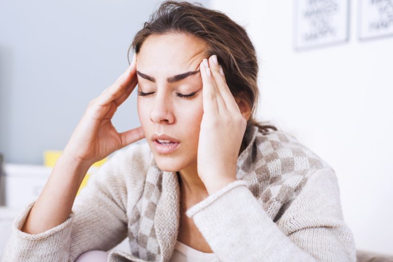 12-18-Autogene training combineren met fysiotherapie bij spierspanningshoofdpijn_374246986 Jonge dame zit aan tafel met last van haar spierspanningshoofdpijn.