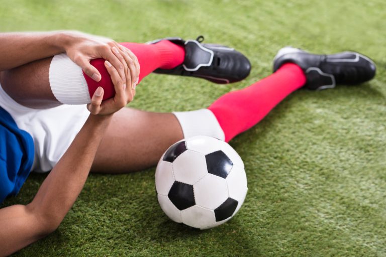 12-2-Verminderde kracht heupspieren verhoogt kans op voorste kruisband letsel_1005702712 Voetballer met zwakke heupmusculatuur ligt op de grond met een knie blessure.