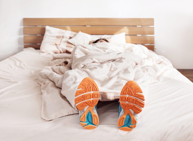 13-10-Regelmatig sporten ondersteunt het bioritme_341368592 Man in bed met loopschoenen aan.