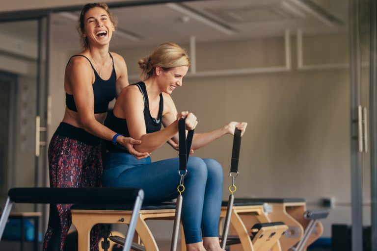 13-14-2x per week Pilates helpt beter maar niet sneller bij rugpijn_1186289119 Twee dames die lachen tijdens het doen van de pilatesoefeningen.