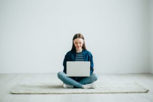 Jonge dame zit op de grond met haar laptop in haar schoot.