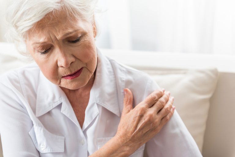 13-18-Het effect van angst en depressie op herstel na rotatorcuff operatie_713128489 Sombere vrouw grijpt schouder vast in verband met post-operatieve pijn.
