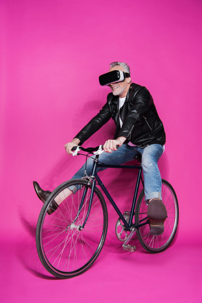 Oudere man met VR-bril op fiets.