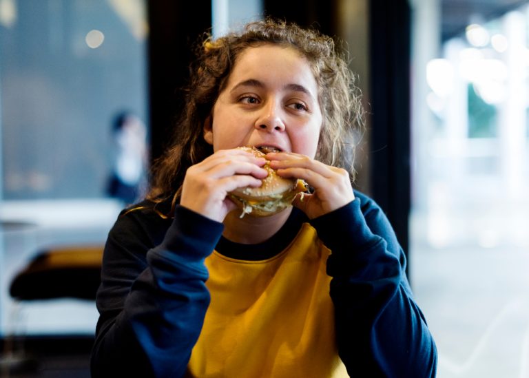 13-9-Musculoskeletale pijn bij adolescenten heeft relatie met ongezond gedrag_1080349724 Adolescente eet hamburger.