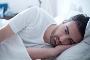 Sombere man met nekpijn ligt wakker.