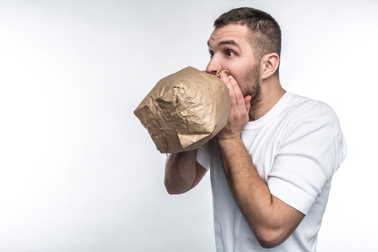 14-07-Korte instructie gaat hyperventilatie tegen bij ademhalingstraining_1060682468 Man ademt in zak zoals bij hyperventilatie weleens gedaan wordt.