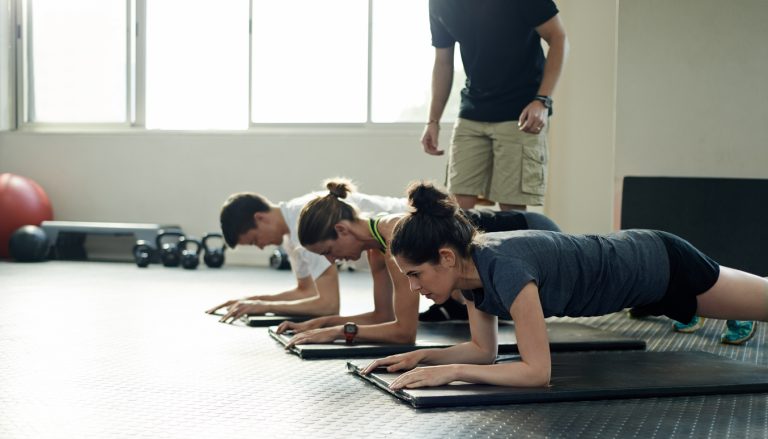 Shot of a group of young people working out on exercise mats while their trainer looks on