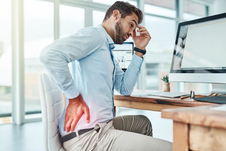 Sitting for long periods of time can strain your body Shot of a young businessman suffering with back pain while working in an office
