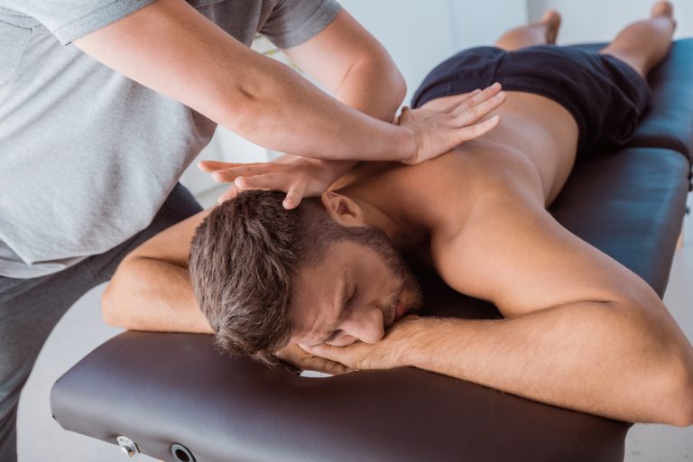 Close-up of a physical therapist giving back massage to a man lying on bed at rehab center