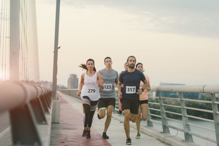 Marathon Runners. Runners running marathon in the city. They are running over the bridge at sunset. Wearing numbers on their sport clothes. Cityscape in background.
