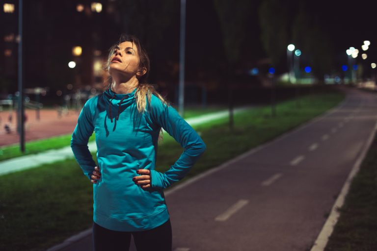 After running Young tired woman standing on the running track outdoor after running. It's night time.