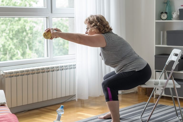 Senior women exercise at home Senior woman holding a towel and stretching while sitting on chair.