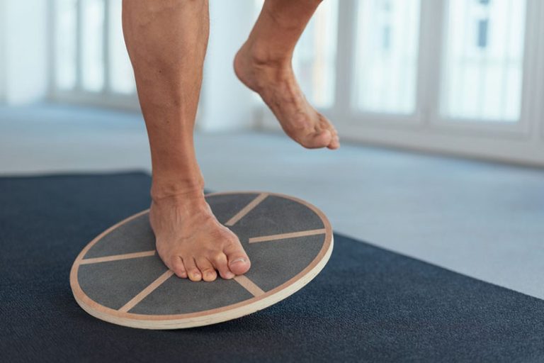 Man Man strengthening his leg muscles working out using a balance board in a gym in a close up view on his feet and equipment