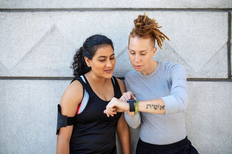 Sporty women checking fitness app on smart watch Two sporty women wearing sportswear working out outdoors in the city having a break and looking at smartwatch. Female friends looking at fitness tracker.