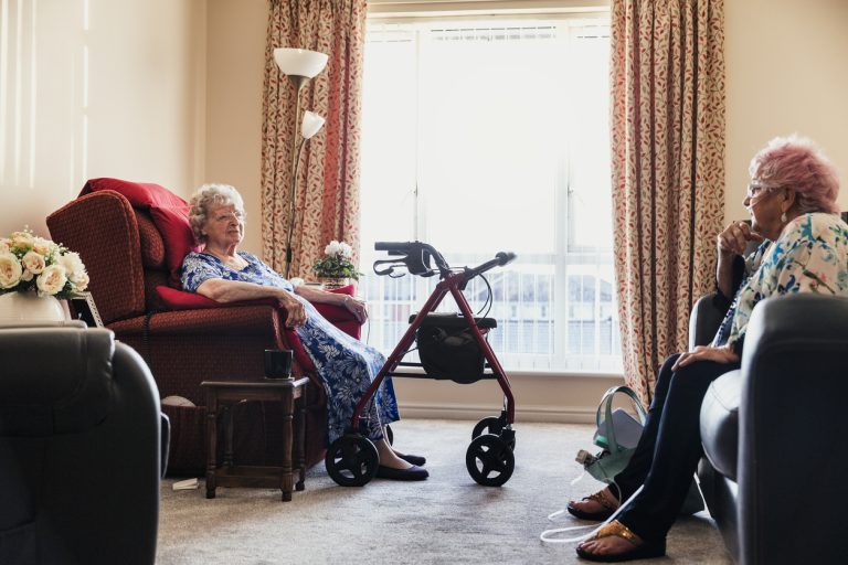 Senior Friends Socialising in a Nursing Home Two senior woman sitting chatting in a nursing home in North East of England. One has pink hair.