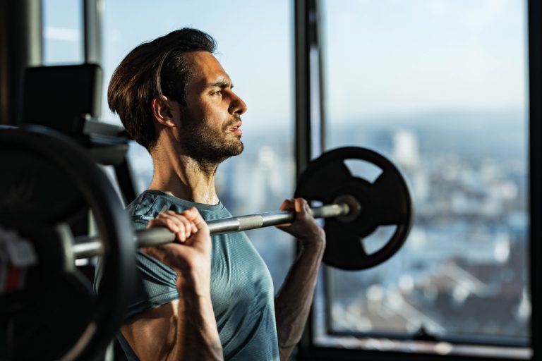 Determined sportsman exercising with barbell in a gym. Determined athletic man having strength exercises with barbell in a gym. Copy space.