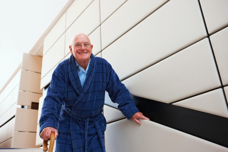 happy senior adult walking down stairs with cane Elderly man in bathrobe walking down the stairs with help of walking stick looking at camera smiling