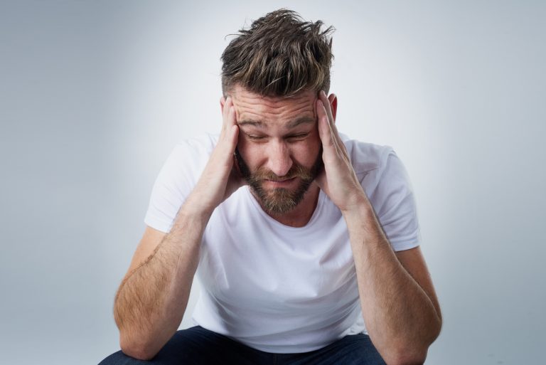 Does anyone have a headache tablet? Shot of a young man with a headache holding his head while sitting on a chair in the studio