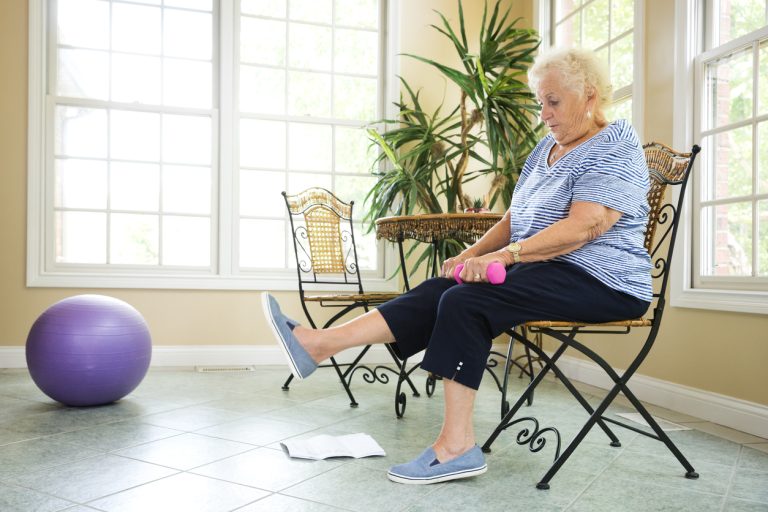 Senior exercising at home Senior Caucasian woman in late 70s performs physical therapy exercises at home to strengthen her arms and legs