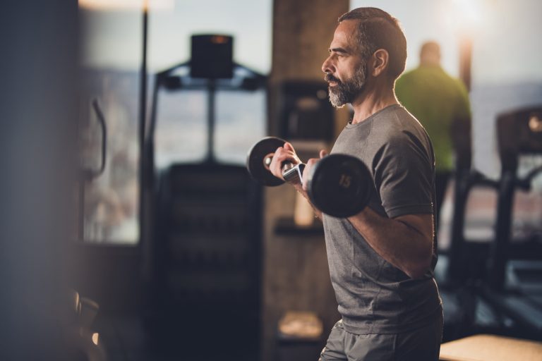 Active senior man having strength exercise with barbell in a gym. Determined mature man exercising with barbell in a health club.