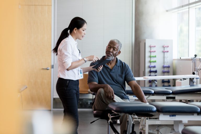 Female doctor talks with senior male patient Attentive senior African American man listens as a female doctor shows him something on a digital tablet about his illness or condition.