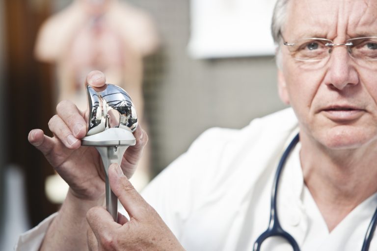 Mature doctor presenting total knee prosthesis A mature medicine presenting total knee prosthesis.