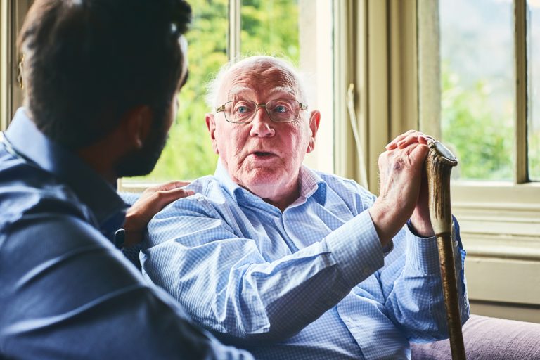 Elderly man talking with doctor at home Elderly man with walking stick talking to doctor at home