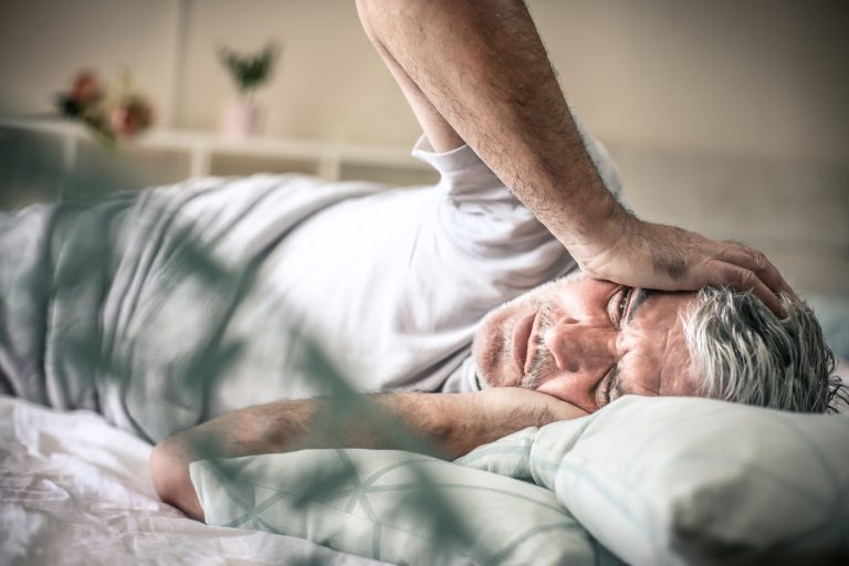 Pain in head. Senior man lying on bed and having headache. Space for copy.