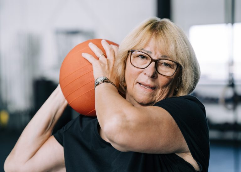Blond senior woman holding medicine ball at gym Portrait of blond senior woman holding medicine ball. Elderly female is doing cross training. She is exercising at gym.