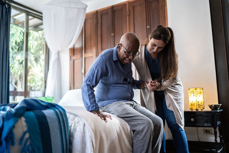 Home caregiver helping a senior man standing up at home Home caregiver helping a senior man standing up at home