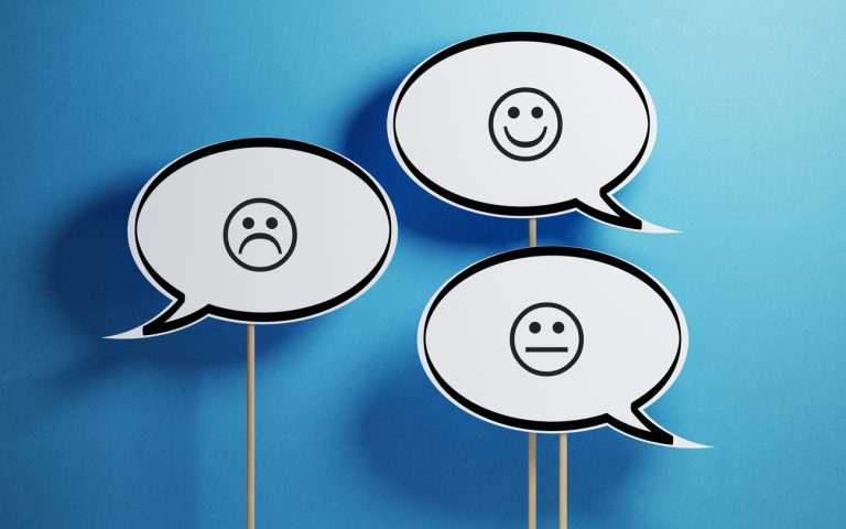 White Chat Bubble With Wooden Stick On Yellow Background White chat bubble with wooden stick on blue background. There are various smiley faces on the speech bubbles. Horizontal composition with copy space.