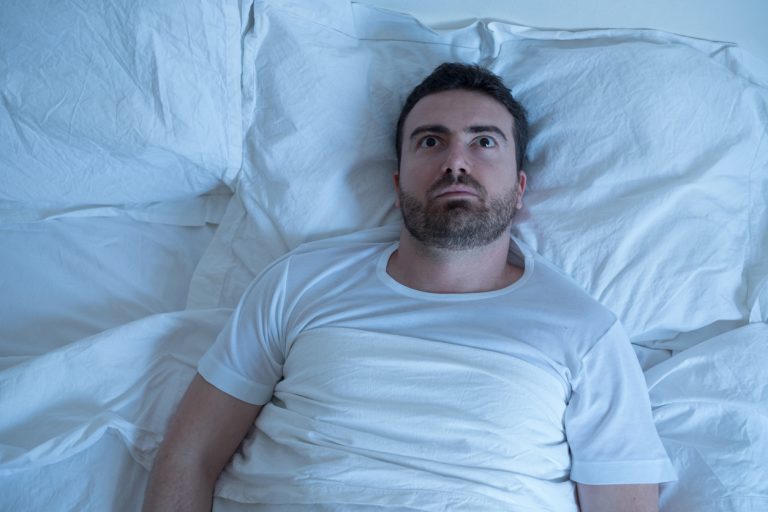 Thoughtful man trying to sleep in his bed at night Stressed man trying to sleep in his bed at night