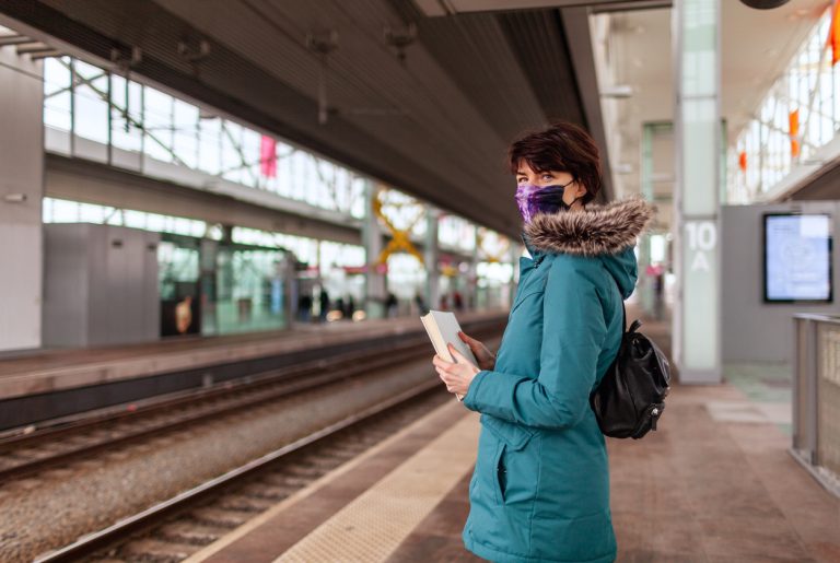 Young woman in blue raincoat on the platform of a railway train station waiting patiently Young 30 year old woman in blue raincoat on the platform of a railway train station waiting patiently