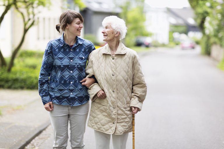 young caregiver helping senior woman walking in the street senior woman