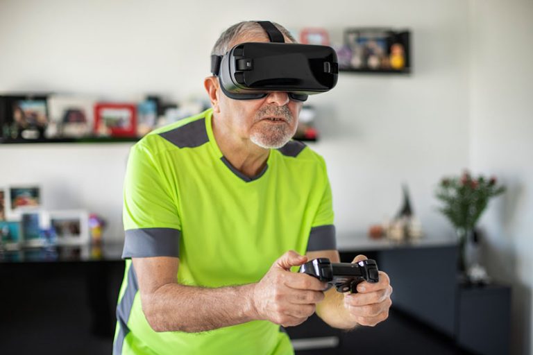 An elderly man plays video football game with virtual reality goggles and joystick Hi-tech concept with vr glasses