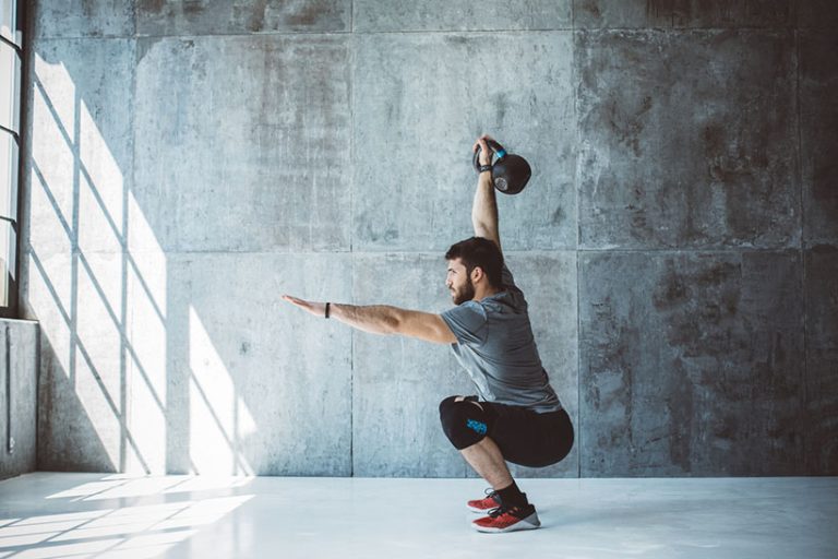 Cross training Male fitness athlete performing overhead squat with kettlebell