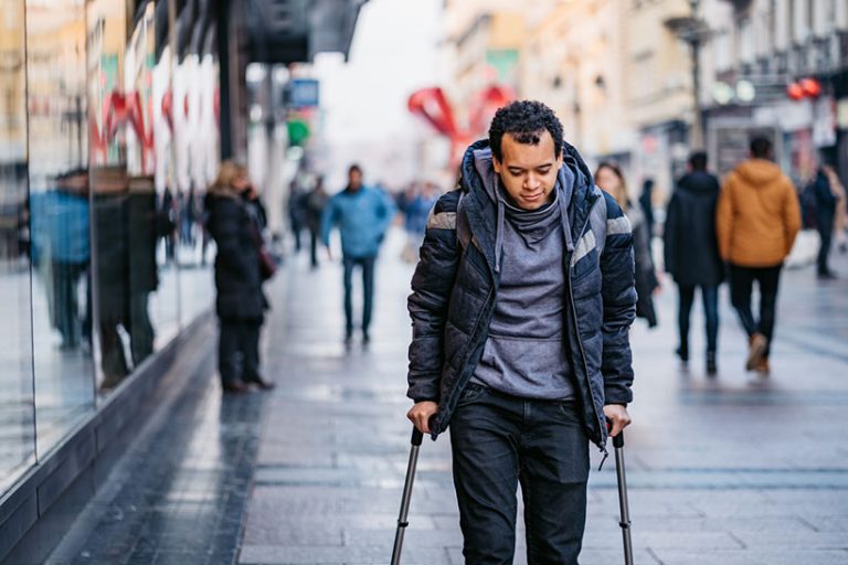 Man using walking canes for walking downtown injured Young mixed raced injured man using walking canes for walking downtown.