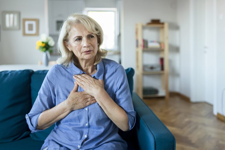 Upset stressed older woman feeling heartache Senior Woman Suffering From Chest Pain While Sitting on Sofa at Home. Old Age, Health Problem, Vision and People Concept. Heart Attack Concept. Elderly Woman Suffering From Chest Pain Indoor