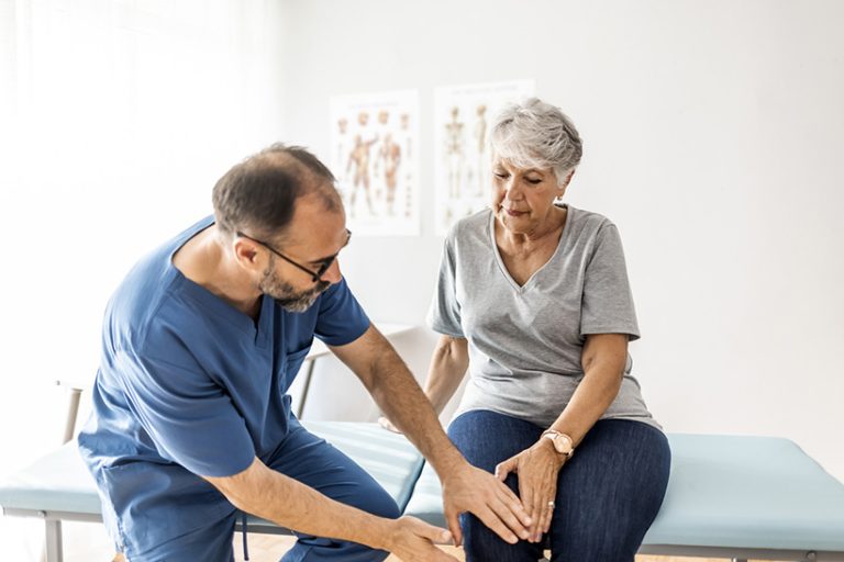 Senior woman having her knee examined by a doctor. Photo of senior woman having some knee pain. She's at doctor's office having medical examination by a male doctor. The doctor is touching the sensitive area and trying to determine the cause of pain.