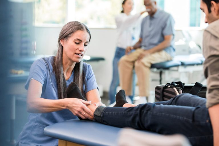 Physical therapist works on man's ankle during physical therapy session A female physical therapist examines a male patient's ankle during a physical therapy session.