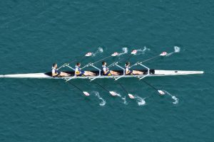 Vier roeiers die synchroon peddelen in een roeiboot, symbool voor interpersoonlijke synchronie en samenwerking
