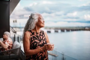 Vrouw kijkt rustig uit over het water en lijkt bewust te genieten van het moment. Een illustratie van lichaamsbewustzijn en zelfregulatie uit het psychosomatisch competentiemodel.