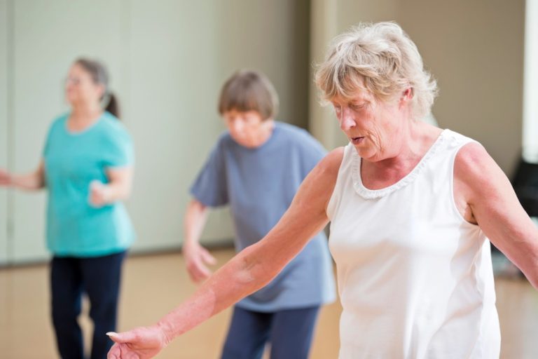 Groep oudere vrouwen die samen dansant bewegen in een oefenzaal als onderdeel van een bewegingsinterventie.