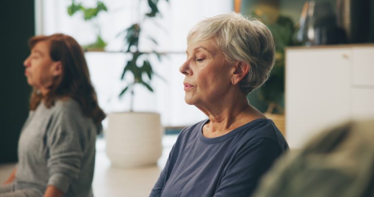 Twee volwassenen oefenen mindfulness in zittende houding tijdens een rustige groepssessie.