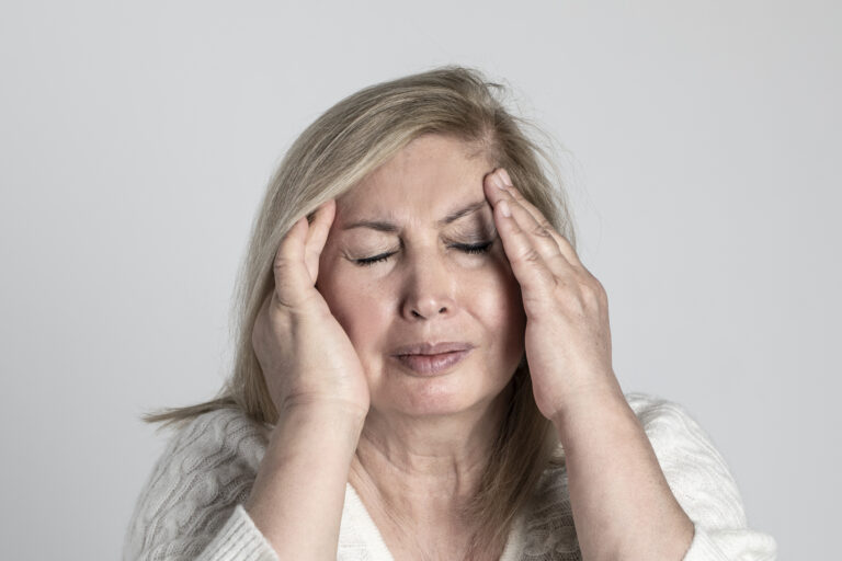 Vrouw met gesloten ogen die met beide handen haar slapen vasthoudt vanwege hoofdpijn.