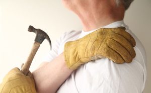 Man met een hamer in hand, die zijn schouder vasthoudt, symboliseert schouder impingement syndroom