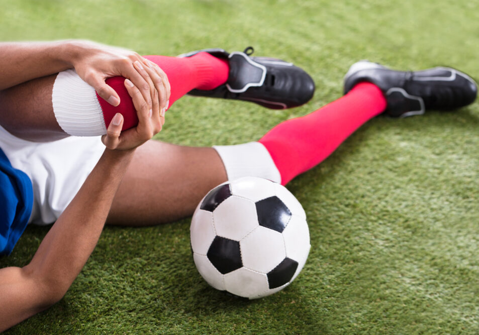 Voetballer met zwakke heupmusculatuur ligt op de grond met een knie blessure.